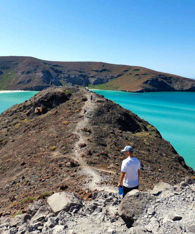 Allan walking on rocks at Balandra Bay, Mexico which he traveled to super cheap.