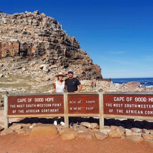 Allan and Katharina standing behind the Cape of Good Hope signpost with the blue ocean in the background.