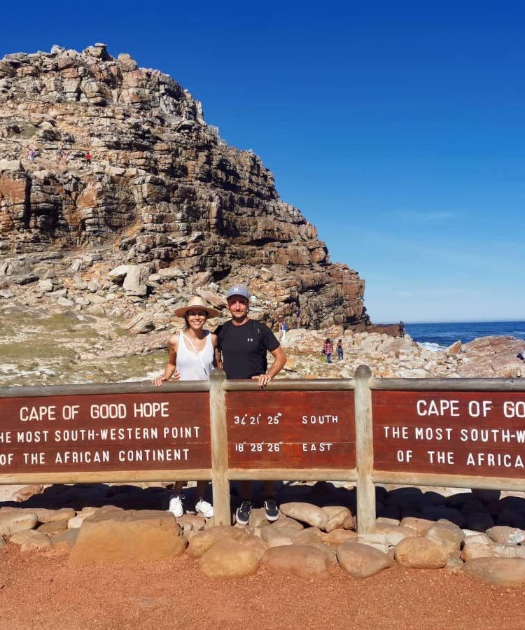 Allan and Katharina standing behind the Cape of Good Hope signpost with the blue ocean in the background.