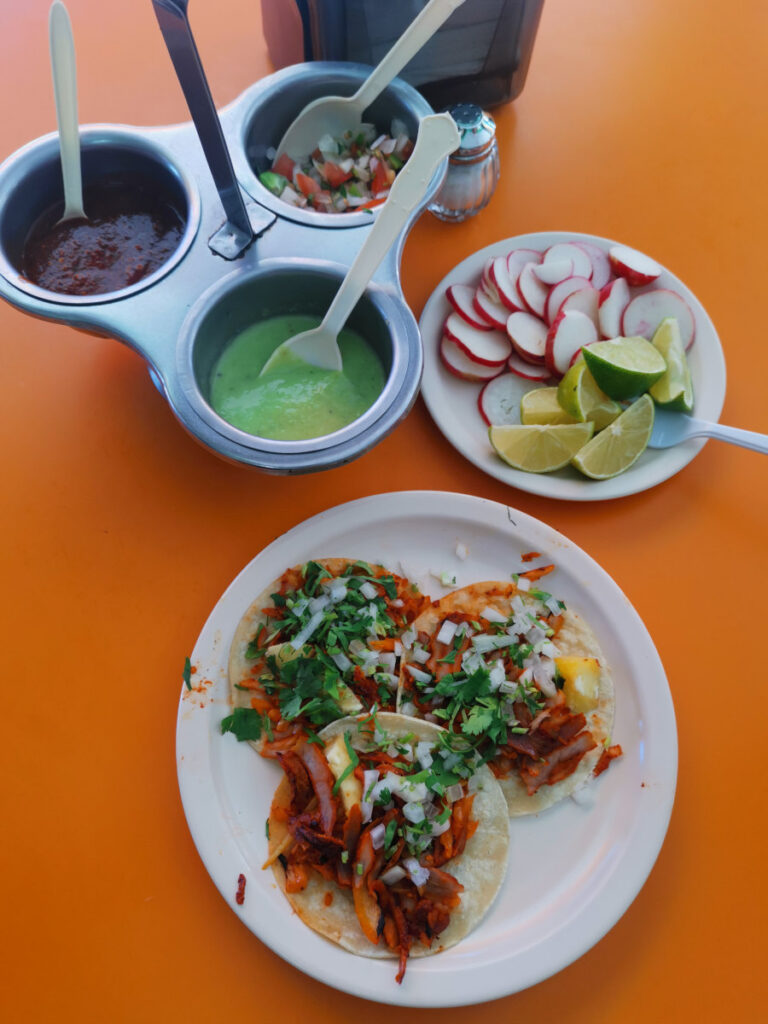 3 pastor tacos from El Fogon on a white plate next to a bowl of limes