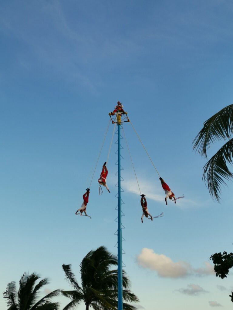 Four men hanging by ropes swinging from a pole near the beach in Playa Del Carmen