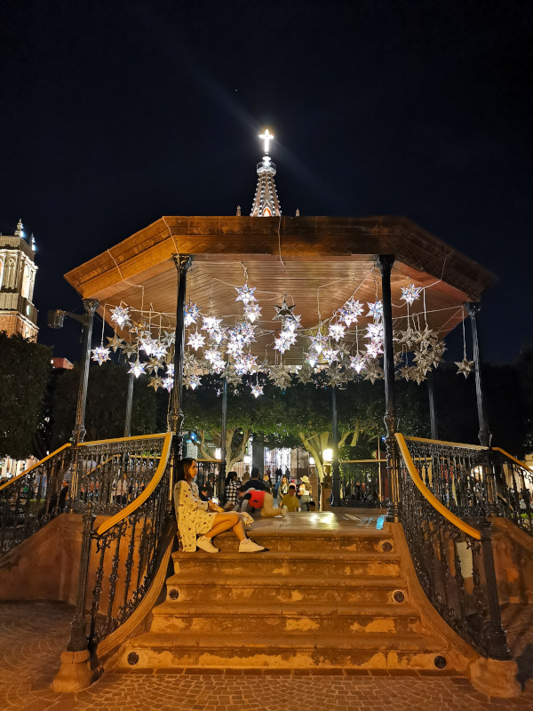 The gazebo lit up with silver stars with the cross of the cathedral in the back