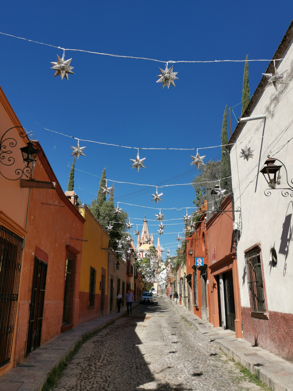 Street with San Miguel de Allende cathedral at the end during day time with lots of silver star lights hung up