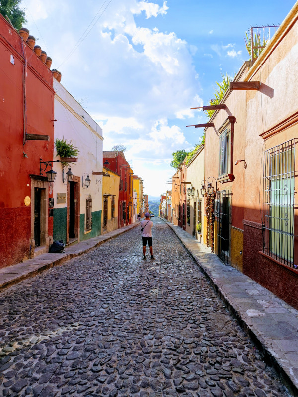 Allan standing in the middle of a cobblestone street taking a photo in San Miguel de Allende