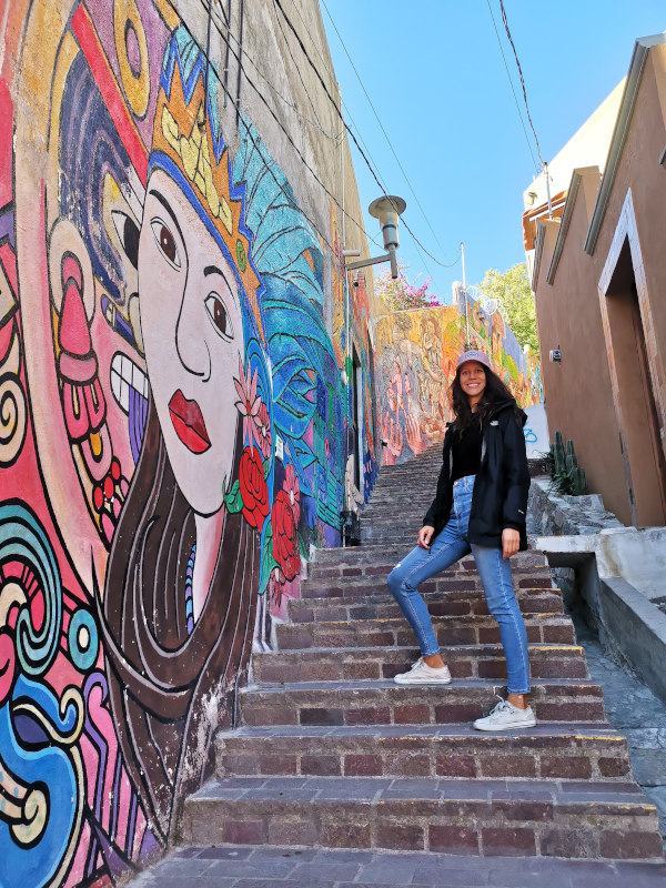 Katharina standing on stairs next to colorful street art in Guanajuato 