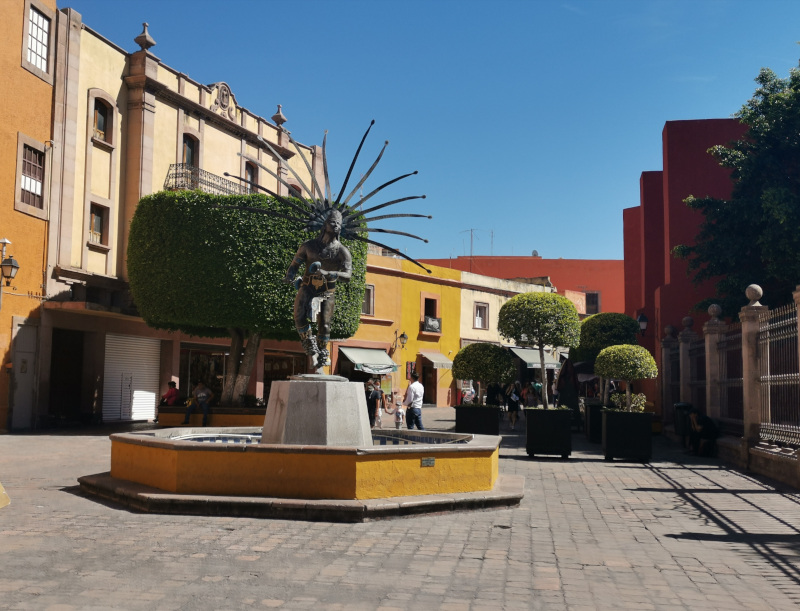 A statue in downtown Querétaro with colorful buildings in the background