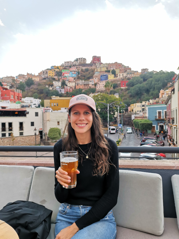 Katharina sitting with a beer on a rooftop in Guanajuato with colorful houses in the back