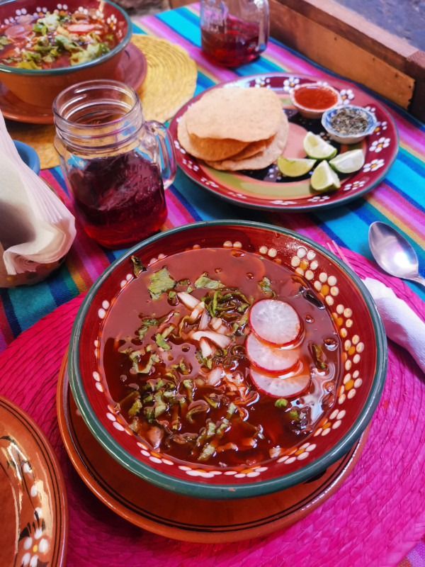 A bowl of Pozole with tortillas on the side on a colorful table cloth at Guanajuatiito
