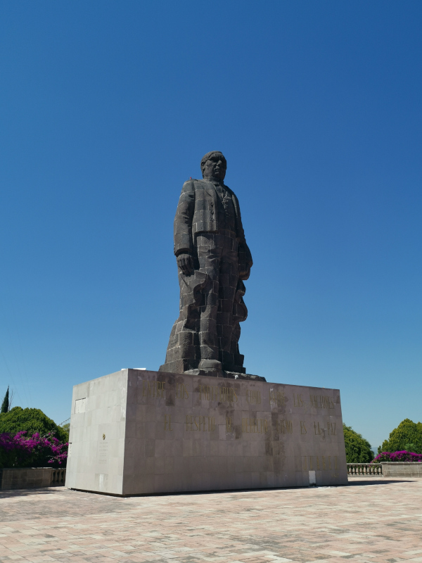 Dark grey statue of Benito Juarez surrounded bz pink flowers
