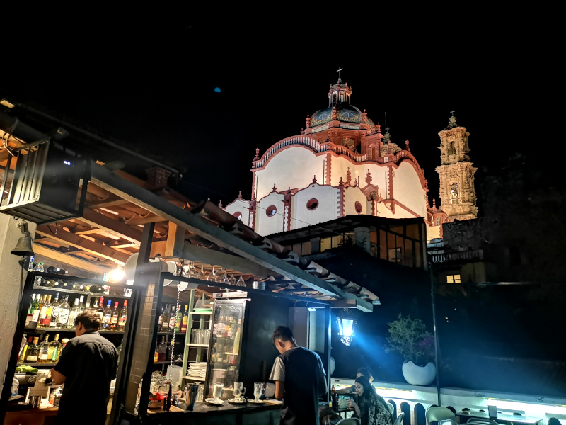 Two bartenders working at the rooftop bar La Casa de los Radios with Taxco's main church in the background