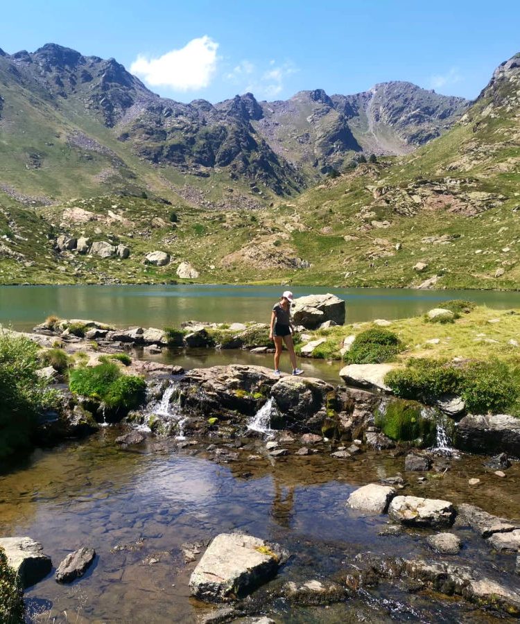 A woman walking across a small waterfall on the Estanys de Tristiana hike