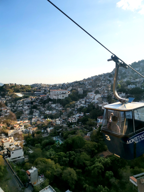 A cable car in Mexico traveling over the top of a town as the sun is setting