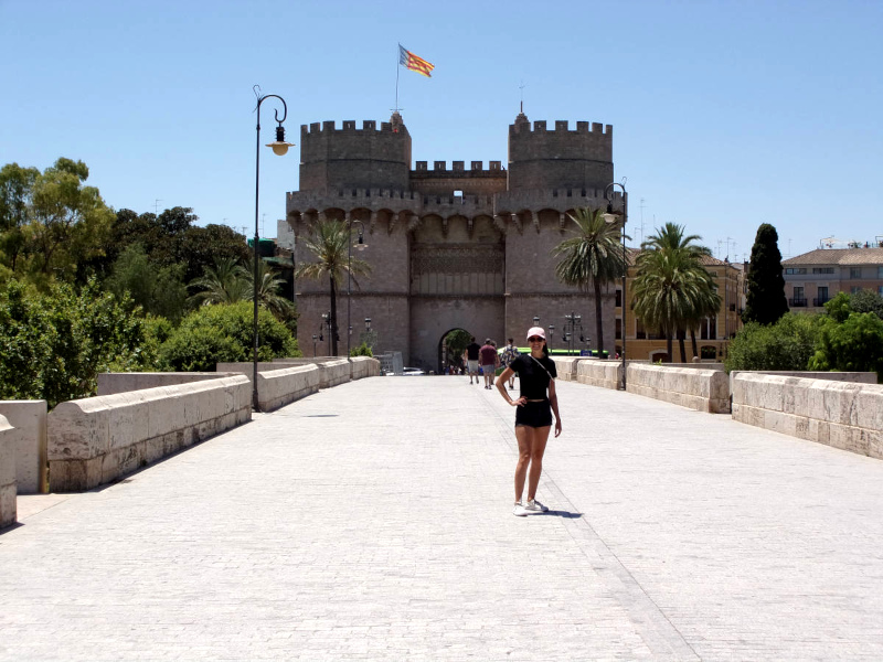 Katharina standing on the Serranos bridge in Valencia, Spain in front of the big tower with a gate