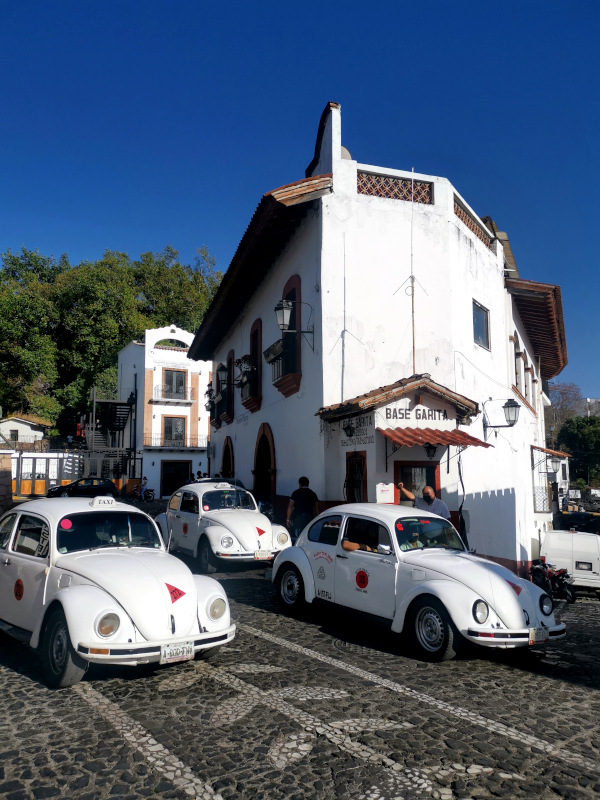 A group of white VW beetles driving down the street - an interesting thing to do in Taxco