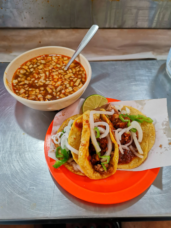 Birria tacos on a plate next to a bowl of soup