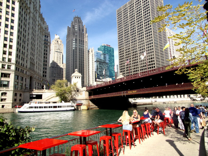 A bar at the River Walk with red chairs  and skyscrapers in the back