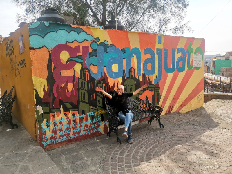 Katharina sitting on a bench in front of a colorful mural with the Guanajuato letter on top