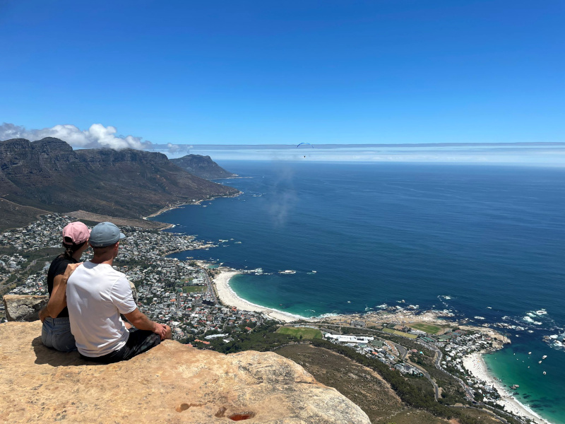 A couple sitting on top of Lions Head looking over the view of beaches from the top of a cliff top a fun activity in Cape Town