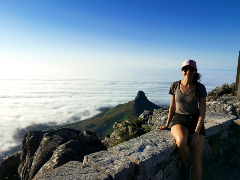 A woman sitting on the summit of Table Mountain with Lions Head in the background