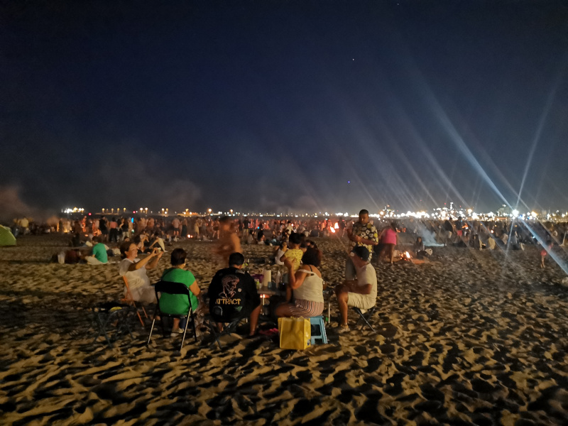 People sitting aorund bonfired on a wide sandy beach