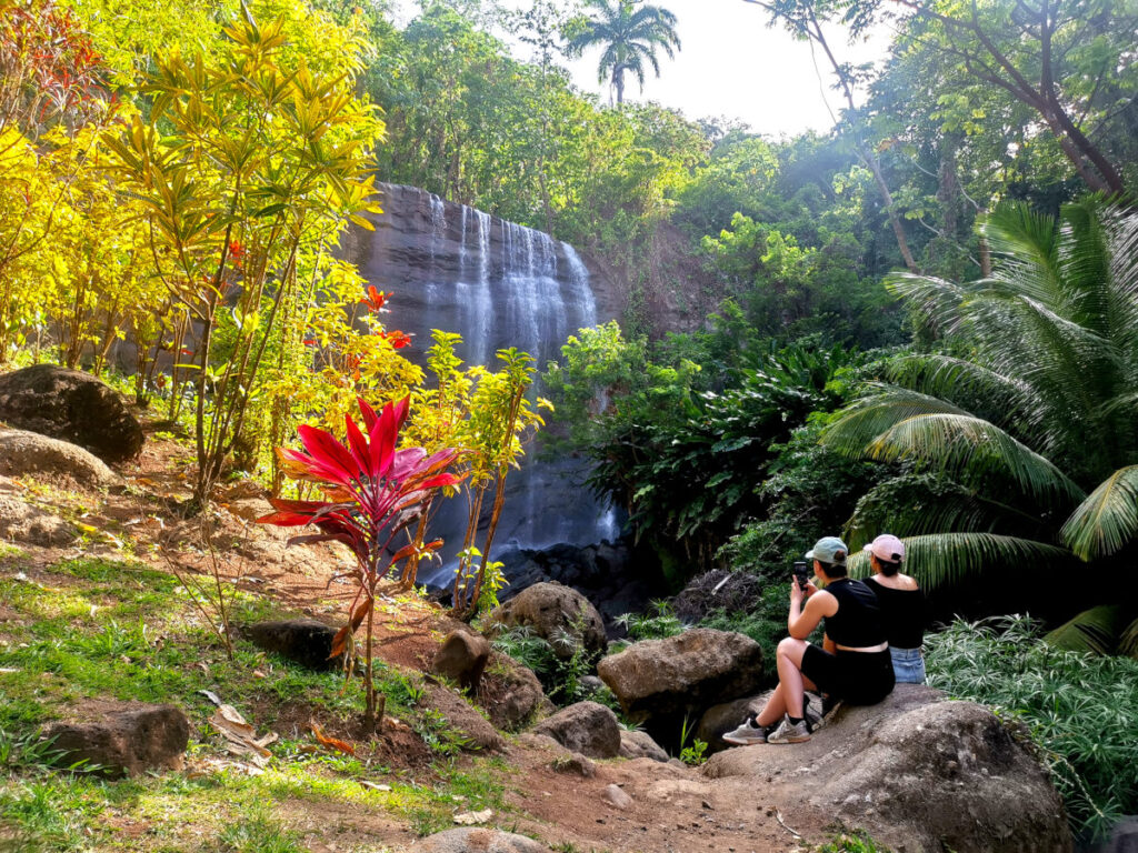 Two woman sitting on a rock in front of Mt Carmel Falls one of the best waterfalls in Grenada