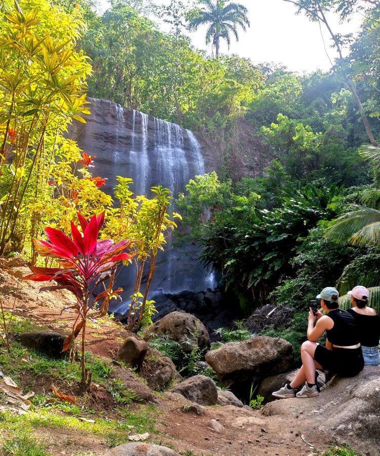 Two woman sitting on a rock in front of Mt Carmel Falls one of the best waterfalls in Grenada