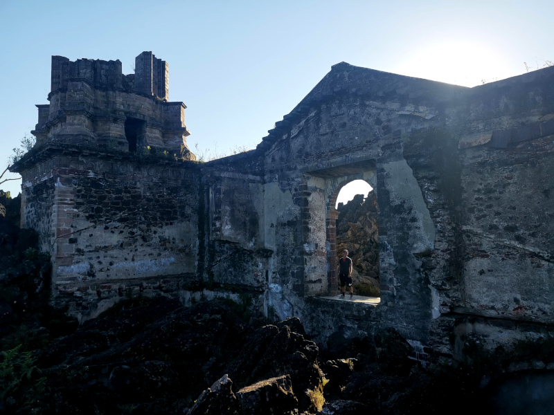 Allan standing in the doorway of a church that has been buried in lava with the sun shining at his back