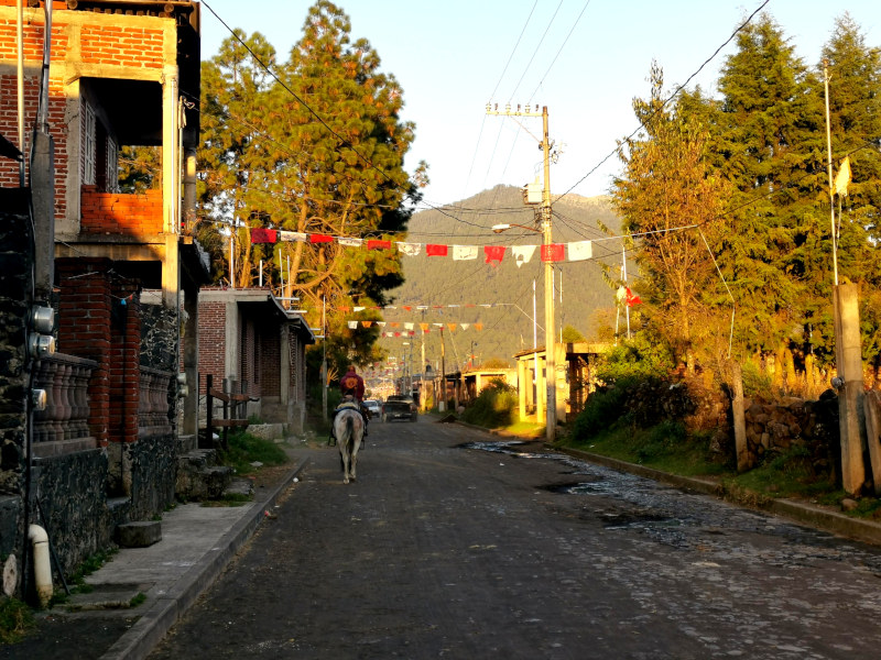 A man in a red sweatshirt riding a horse on a road in Angahuan