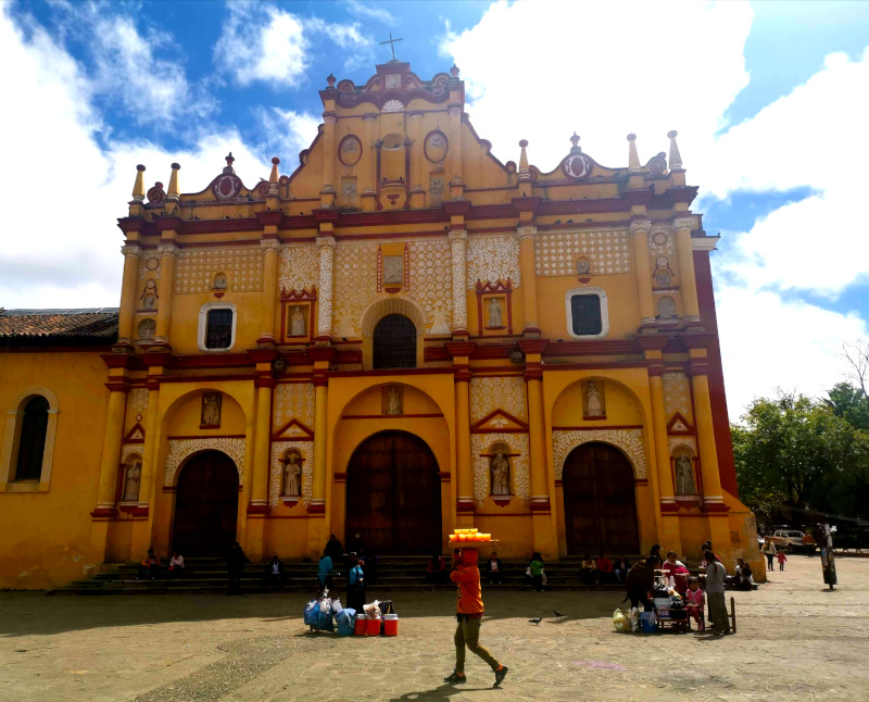 A yellow church in San Cristobal de las Casas with locals walking around in front of it