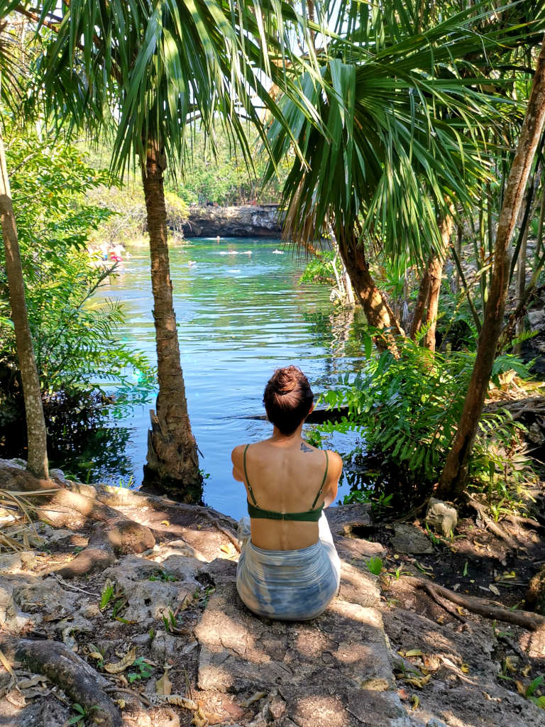 A woman sitting down looking into the waters of cenote jardin del eden one of the best cenotes in playa del carmen