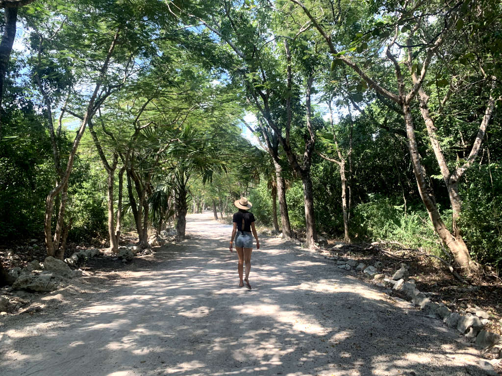 A women with a wide brimmed hat black top and denim shorts walking along the road to cenote jardin del eden one of the best cenotes in playa del carmen