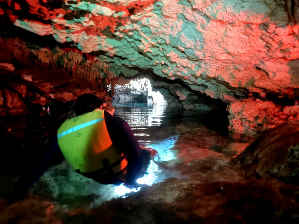A guide wearing a yellow lifejacket making his way through an underwater cave
