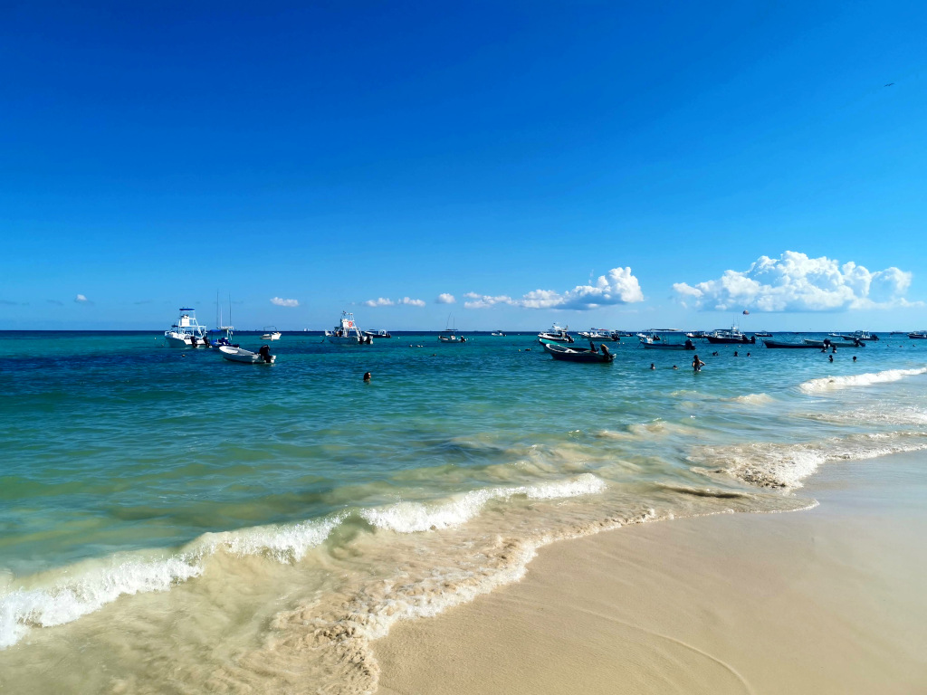 Fishing boats in turquoise blue waters anchored just off the coast of a sandy beach