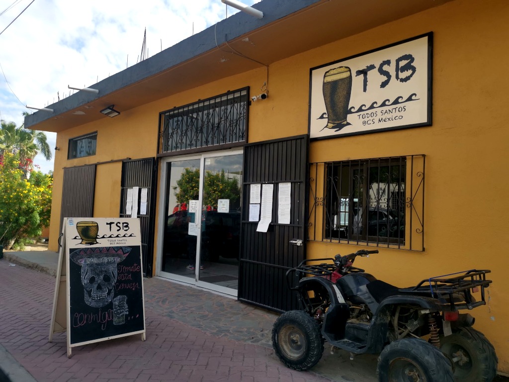 A quadbike parked next to a yellow wall outside of a craft brewery in a beach town