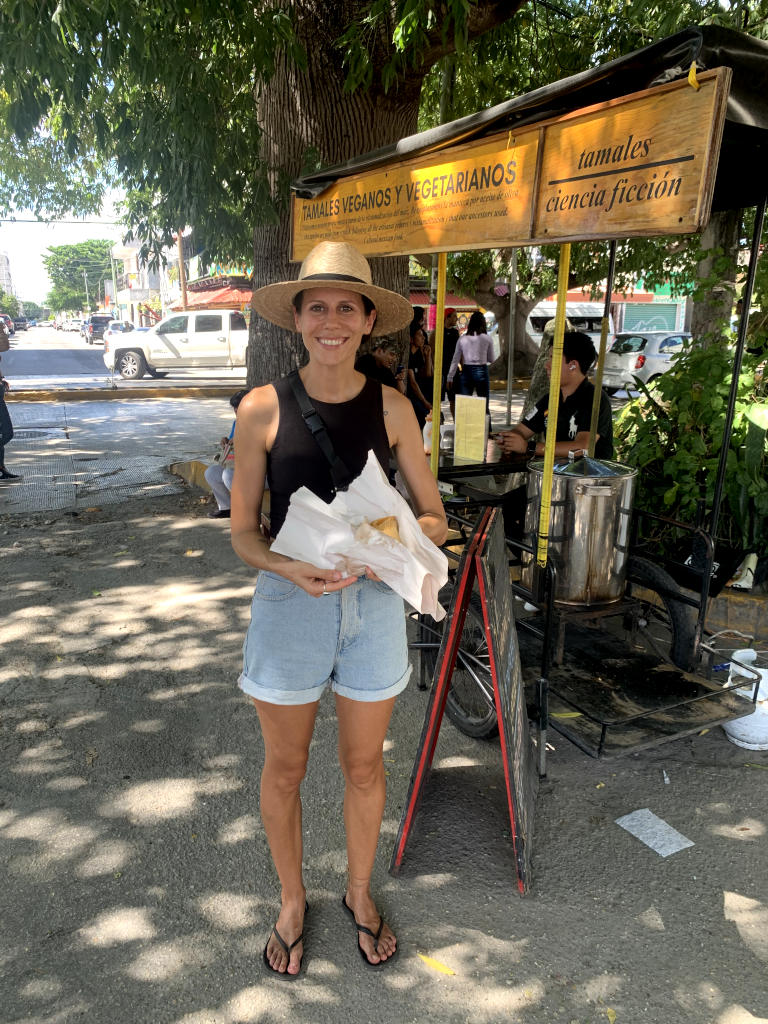 A woman standing in front of a food cart holding a vegan tamale in playa del carmen