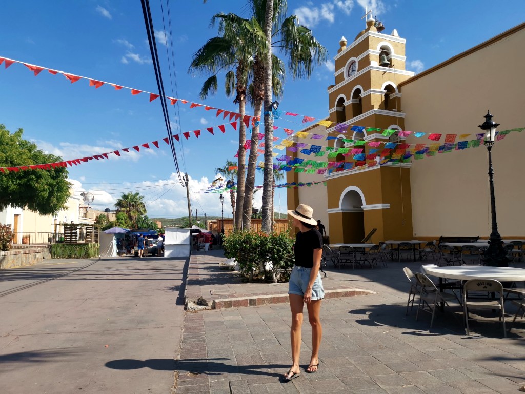 A woman walking on the street under some colorful flas in front of a yellow church in Mexico