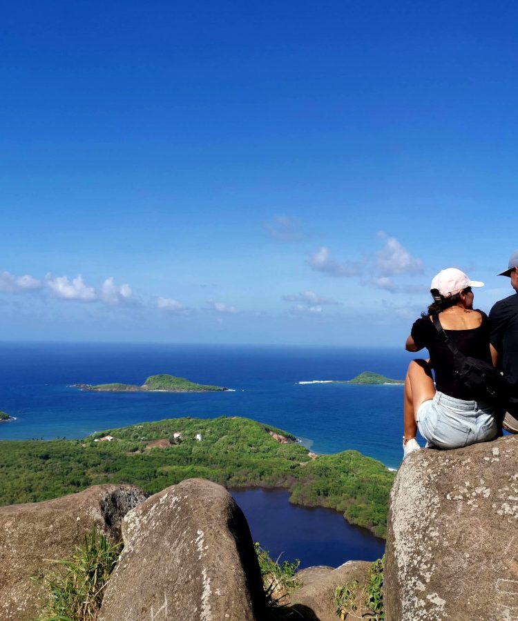 A couple sitting on a rock overlooking the ocean on Welcome Stone Grenada