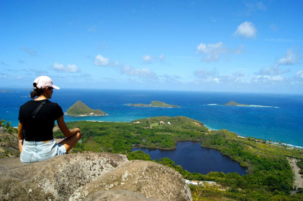 A woman sitting cross legged on a rock overlooking a group of islands from a mountain top at the Welcome Stone Lookout in Grenada