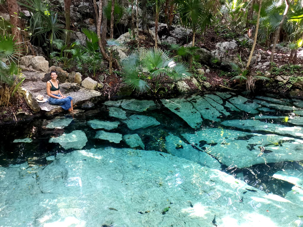 A woman in a sarong sitting next to an open air cenote a great example of what is a cenote in the Yucatan Peninnsula