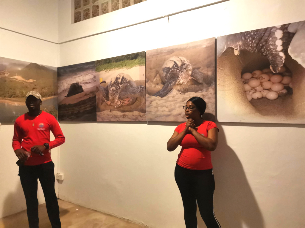 Two guides with red t-shirts on giving on introduction speech for a turtle tour with pictures of turtles on the wall behind them