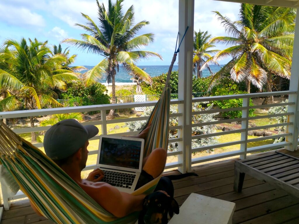 A man sitting in the hammock with a laptop overlooking the ocean deciding which travel insurace for digital nomads to choose