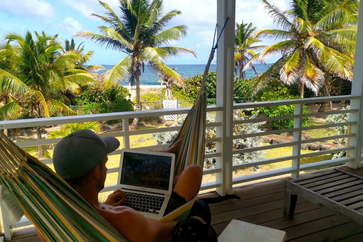 A man sitting in the hammock with a laptop overlooking the ocean deciding which travel insurace for digital nomads to choose