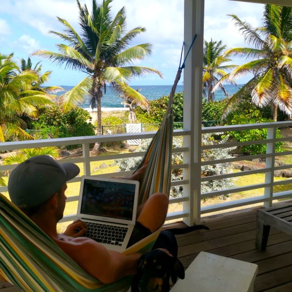 A man sitting in the hammock with a laptop overlooking the ocean deciding which travel insurace for digital nomads to choose