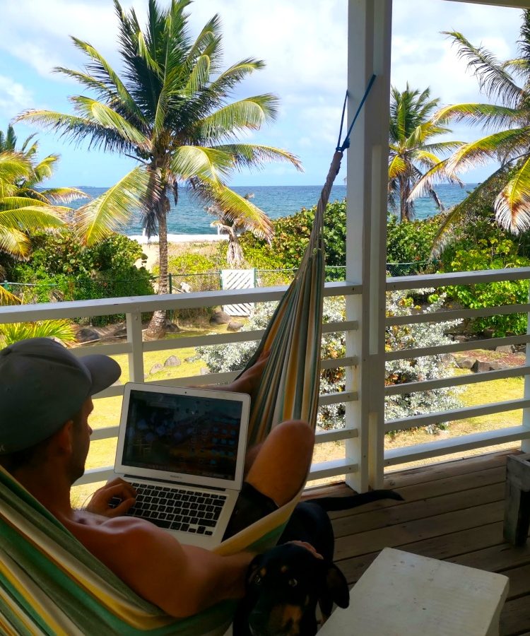 A man sitting in the hammock with a laptop overlooking the ocean deciding which travel insurace for digital nomads to choose