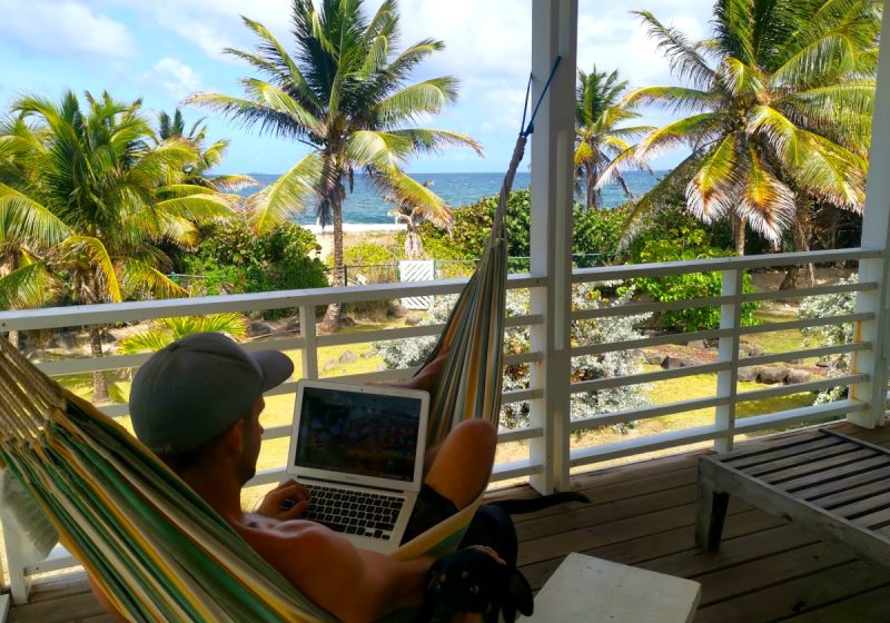 A man sitting in the hammock with a laptop overlooking the ocean deciding which travel insurace for digital nomads to choose