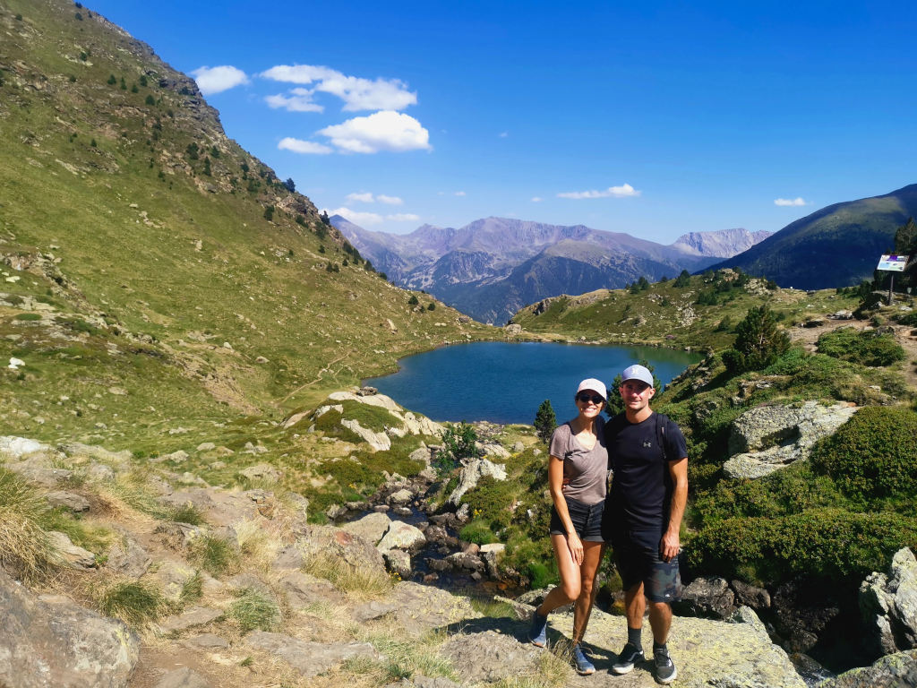 A couple posing in front of a green valley while on a hike in the mountains of Andorra - a free way to travel