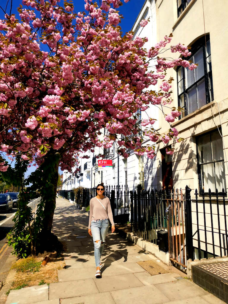 A woman going for a self-guided walk in London underneath a tree covered in pink flowers