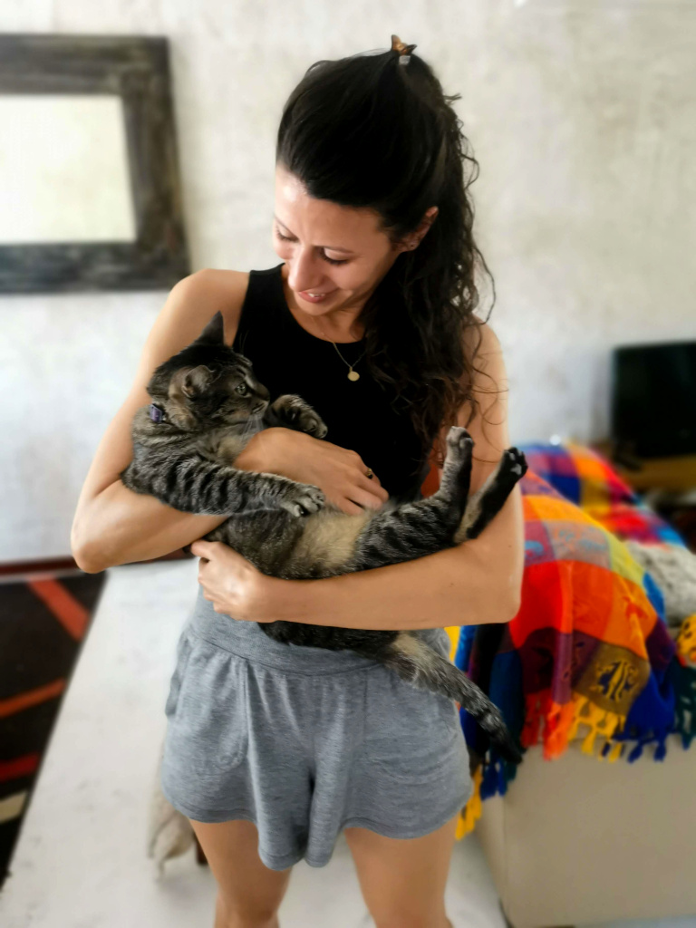 A woman in a black singlet and grey shirts holding a black and grey cat in her hands while petsitting via Trusted House Sitters in Mexico