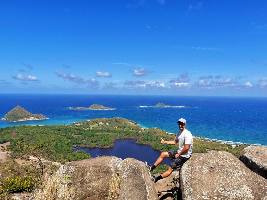 Allan sitting on top of Welcome Stone Lookout with the blue ocean and sky in the background