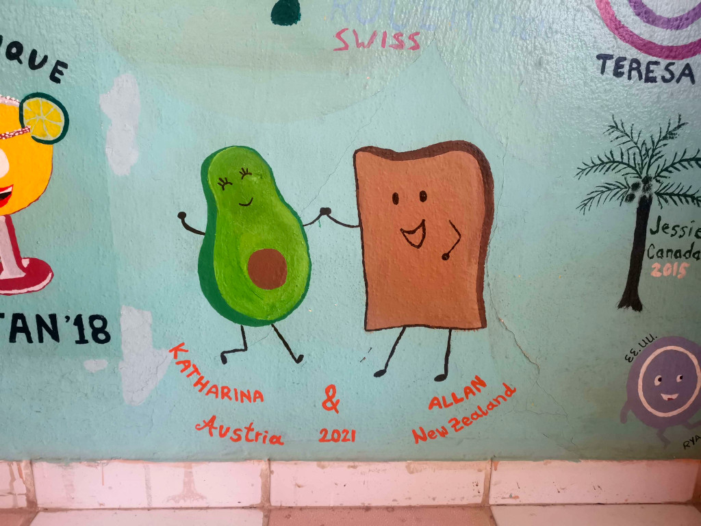 A picture of an avocado and a piece of bread on a wall with arms so that they are holding hands